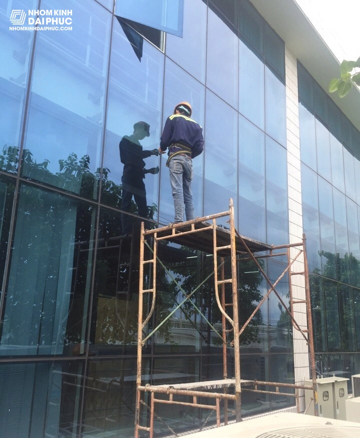 Đội ngũ kỹ thuật đang lắp đặt vách kính lớn tại một nhà xưởng, tuân thủ các quy định an toàn lao động
